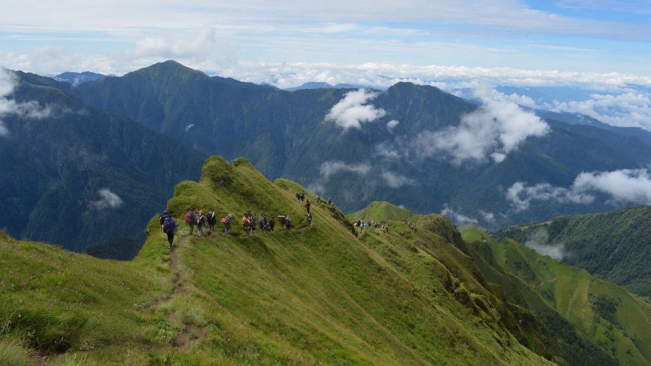 Trekking group walking a green ridge above the clouds, Badimalika, far-western Nepal